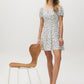 Snow White Ditsy Print Mini Dress - Woman Wearing Off-the-Shoulder Tiered Dress - Suzy Shier
